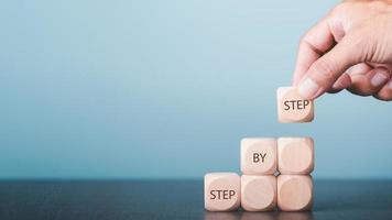 Hands arrange wooden blocks stacked into steps and display messages Step By Step. Business ideas for ladder of personal success, success and growth. photo