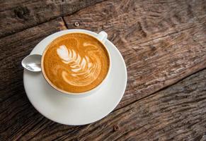 A cup of hot coffee with latte art on the surface serve on the wooden table. photo