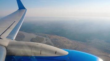 View from the porthole on the engine and wing of the aircraft in flight. The airliner flies high above the terrain, the view from the window video