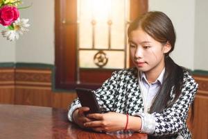 una joven estudiante chatea en línea con su amiga en el teléfono móvil, las redes sociales y el concepto de conexión de chat, la luz del sol a través de las ventanas copia espacio para texto individual foto