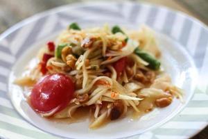 Thai papaya salad on a plate, papaya salad with poop, lemon, pepper, red tomato in white bowl on wooden table photo
