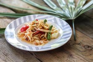 Thai papaya salad on a plate, papaya salad with poop, lemon, pepper, red tomato in white bowl on wooden table photo