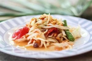 Thai papaya salad on a plate, papaya salad with poop, lemon, pepper, red tomato in white bowl on wooden table photo