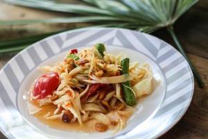 Thai papaya salad on a plate, papaya salad with poop, lemon, pepper, red tomato in white bowl on wooden table photo