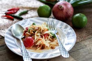 Thai papaya salad on a plate, papaya salad with poop, lemon, pepper, red tomato in white bowl on wooden table photo