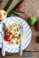Thai papaya salad on a plate, papaya salad with poop, lemon, pepper, red tomato in white bowl on wooden table photo