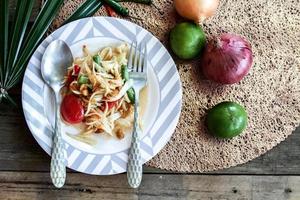 Thai papaya salad on a plate, papaya salad with poop, lemon, pepper, red tomato in white bowl on wooden table photo