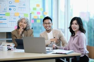 Group of Asia young creative people in smart casual wear smiling in creative office workplace. Diverse Asian male and female stand together at startup. Coworker teamwork concept. photo