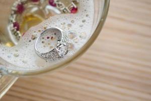 cleaning vintage jewelry diamond ring and bracelet in glass on wood table background photo