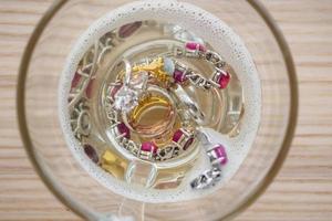 cleaning vintage jewelry diamond ring and bracelet in glass on wood table background photo