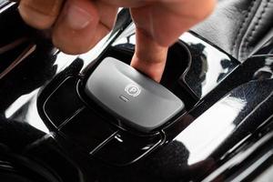Hand push on electronic handbrake button in luxury modern car photo