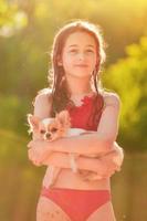 una adolescente con traje de baño rojo y un chihuahua blanco en los brazos. vacaciones de verano junto al río. foto