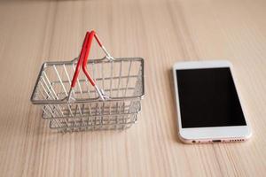 teléfono móvil con cesta en el fondo de la mesa de madera concepto de compras en línea foto
