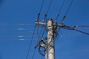 Electric pole power lines outgoing electric wires againts on cloud blue sky. photo