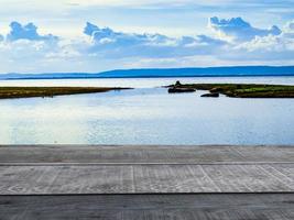 Old wooden table shelf, lake and mountain scenery backdrop, cloudy sky. photo