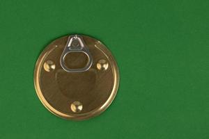 Tin can lid with opener, golden color on a green background. photo