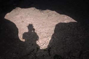 sombra de un hombre en un día soleado tomando una foto de su sombra mientras está de pie sobre la entrada de una cueva.