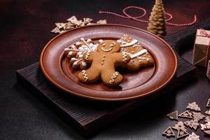 Beautiful gingerbread on a brown ceramic plate with Christmas tree decorations on a dark concrete background photo