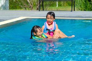 las hermanitas felices juegan en la piscina al aire libre del complejo tropical durante las vacaciones familiares de verano. niños aprendiendo a nadar. actividades saludables de verano para niños. foto