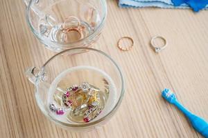 cleaning jewelry diamond ring with glass of hot water and dishwashing liquid on wood table background photo