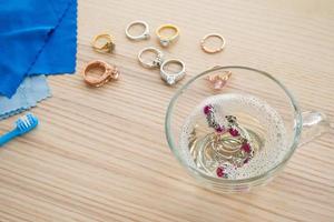 cleaning jewelry diamond ring with glass of hot water and dishwashing liquid on wood table background photo