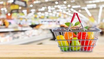 cesta de la compra con frutas en la mesa de madera sobre el fondo borroso del supermercado de la tienda de comestibles foto