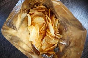 Potato chips in open snack bag close up on table floor photo