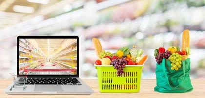 supermarket aisle blurred background with laptop computer and shopping cart on wood table grocery online concept photo