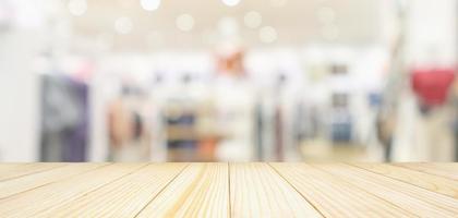 Empty wood table top with modern clothing store interior blur abstract defocused background with bokeh light for product display photo