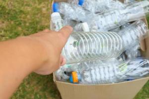 sostenga con la mano y coloque botellas de plástico en una caja de basura de reciclaje marrón foto