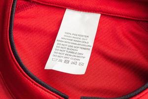 White laundry care washing instructions clothes label on red jersey polyester sport shirt photo