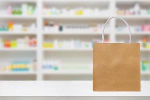 Paper bag on Pharmacy drugstore counter table with medicine and healthcare product on shelves blur background photo