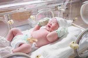 Newborn baby girl inside incubator in hospital post delivery room photo