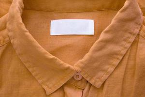 White blank clothing tag label on brown linen shirt fabric texture background photo