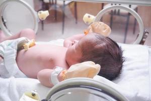 Newborn baby girl inside incubator in hospital post delivery room photo