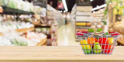 Shopping basket with fruit on wood table over grocery store supermarket blur background photo