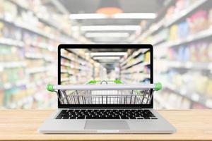 supermarket aisle blurred background with laptop computer and shopping cart on wood table grocery online concept photo