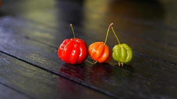Three Brazilian red cherries on a dark table with blurred background photo