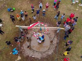 Blitar, Indonesia - September 11th 2022 Aerial view of housewife who is taking part in a banana tree climbing competition to get a prize and is seen by many people photo