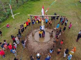 Blitar, Indonesia - September 11th 2022 Aerial view of housewife who is taking part in a banana tree climbing competition to get a prize and is seen by many people photo