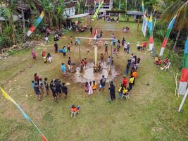 Blitar, Indonesia - September 11, 2022 Aerial view of very happy children taking part in a banana tree climbing competition to get prizes and being seen by many photo