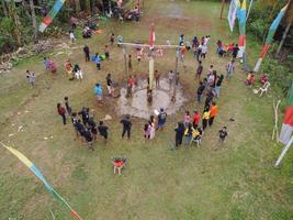 Blitar, Indonesia - September 11, 2022 Aerial view of very happy children taking part in a banana tree climbing competition to get prizes and being seen by many photo