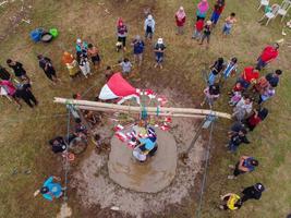 Blitar, Indonesia - September 11th 2022 Aerial view of housewife who is taking part in a banana tree climbing competition to get a prize and is seen by many people photo