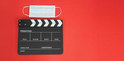 Clapper board or movie slate with face mask or medical mask isolated. it use in film,movies production and cinema industry on red background.Covid-19 or social distance concept. photo