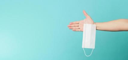 Hands holding white surgical face mask.Medical mask on blue and green or Tiffany Blue background. photo