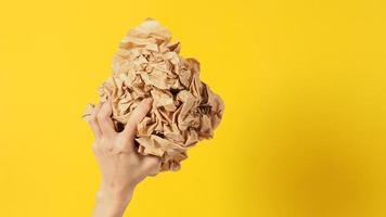 The woman's hands is holding crumpled brown paper ball on yellow background. photo