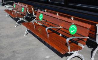las pegatinas de puntos verdes se colocan en una silla de parque de madera para mostrar a las personas dónde pueden sentarse mientras mantienen el distanciamiento social. foto