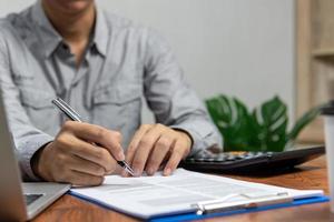 mano que sostiene la pluma que escribe papeleo documento comercial inversión financiera o contrato de firma trabajo y seguro en el escritorio. foto