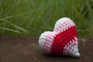 Crochet varicolored heart shape made from yarn being left alone in the garden for Valentine's day. photo