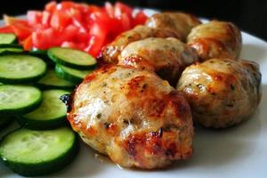 Traditional Cypriot food.  Sheftalia Cypriot Lamb and Pork Sausages. Grilled Sausages with Fresh Vegetables included cucumber and tomato on a white plate. photo